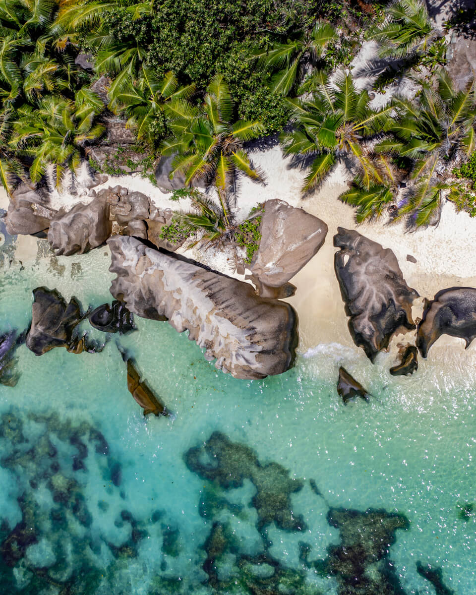 drone photo of a beautiful beach in the Seychelles with white sand, green palm trees, blue water and dark granite rocks, seychelles Itinerary and travel tips